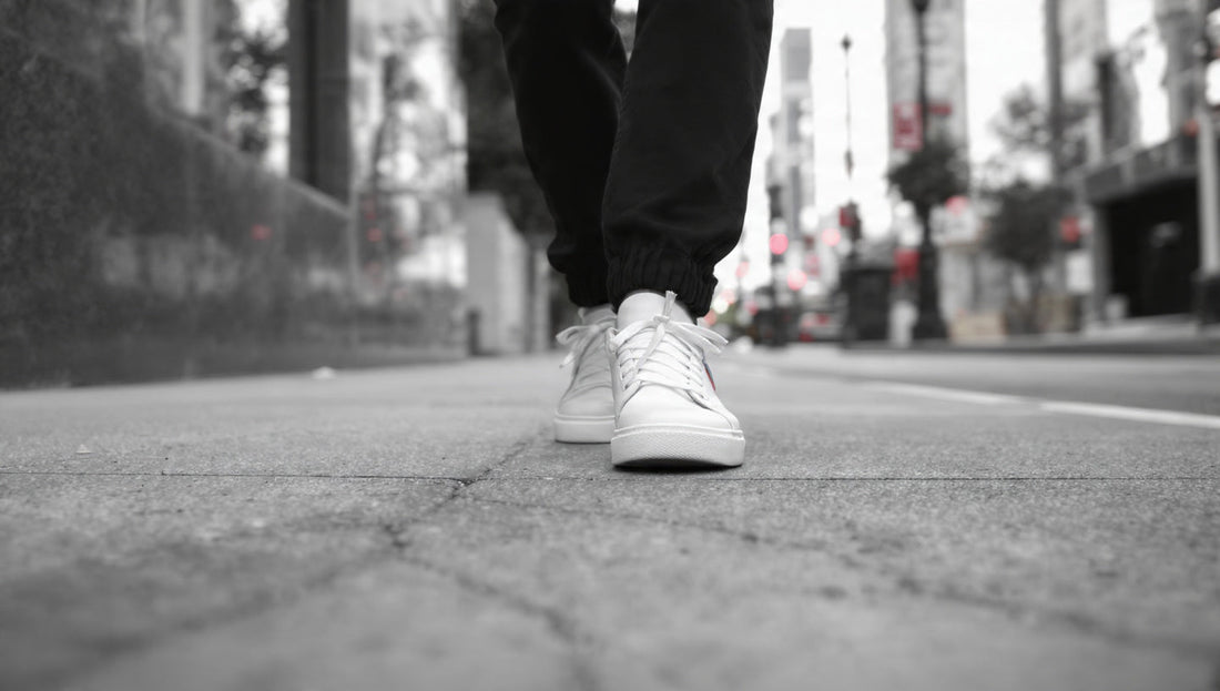 Personne en baskets blanches marchant sur un trottoir urbain, style éditorial noir et blanc