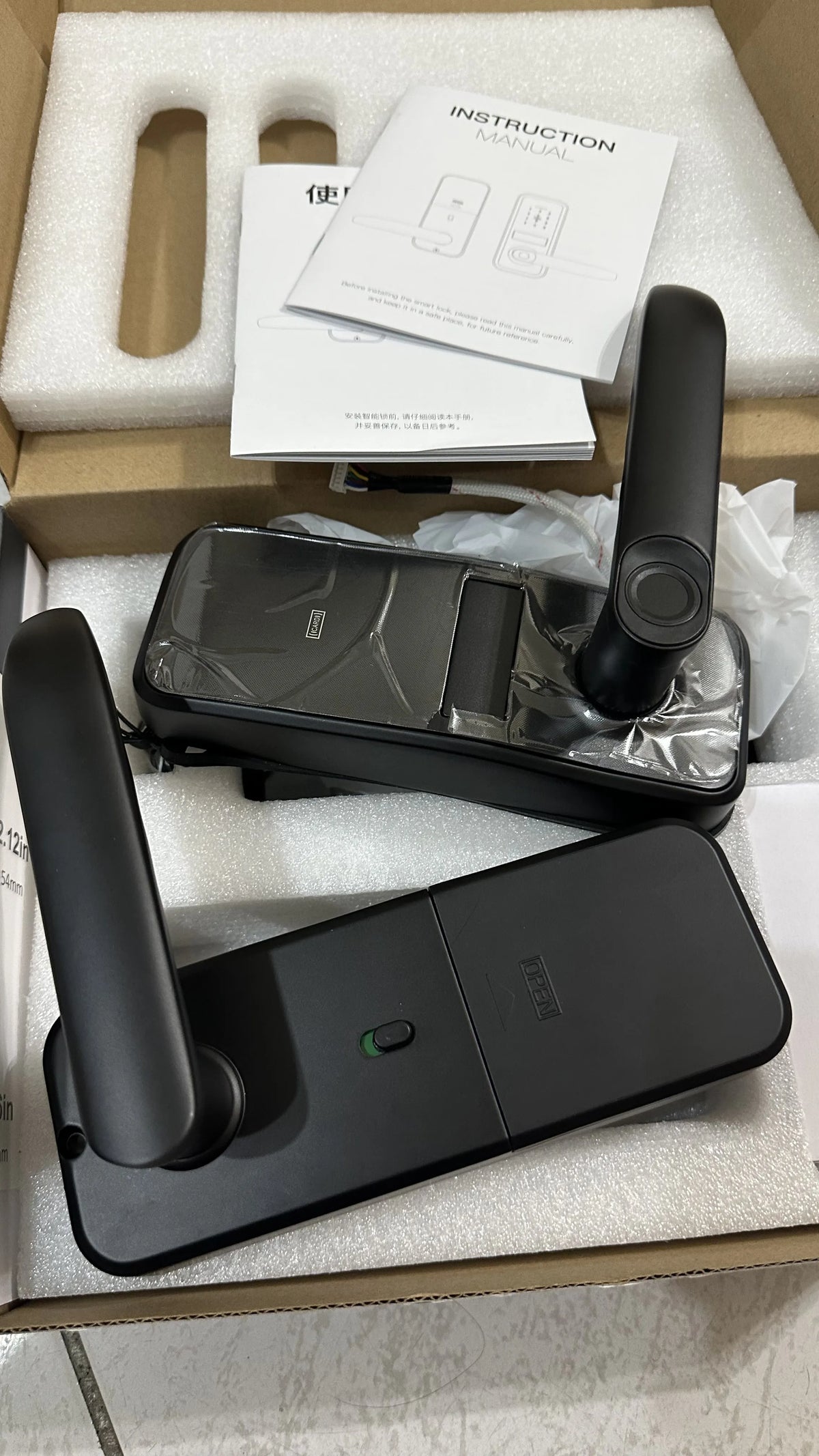 Lever-handle smart door lock unboxed, showing both panels, handles and the printed instructions
