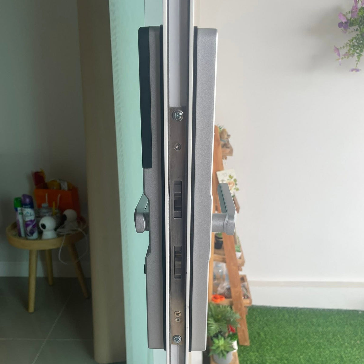 Silver smart door lock fitted to a white framed glass door, living room behind