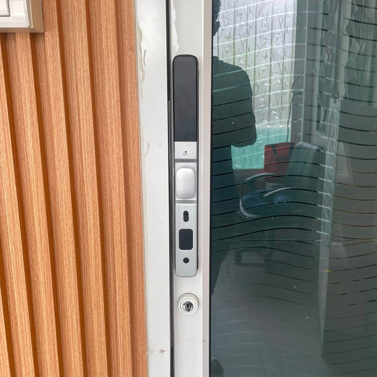 Silver short-handle smart door lock on a glazed door beside a timber slat wall