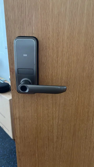 Black lever-handle smart door lock fitted to a light oak door