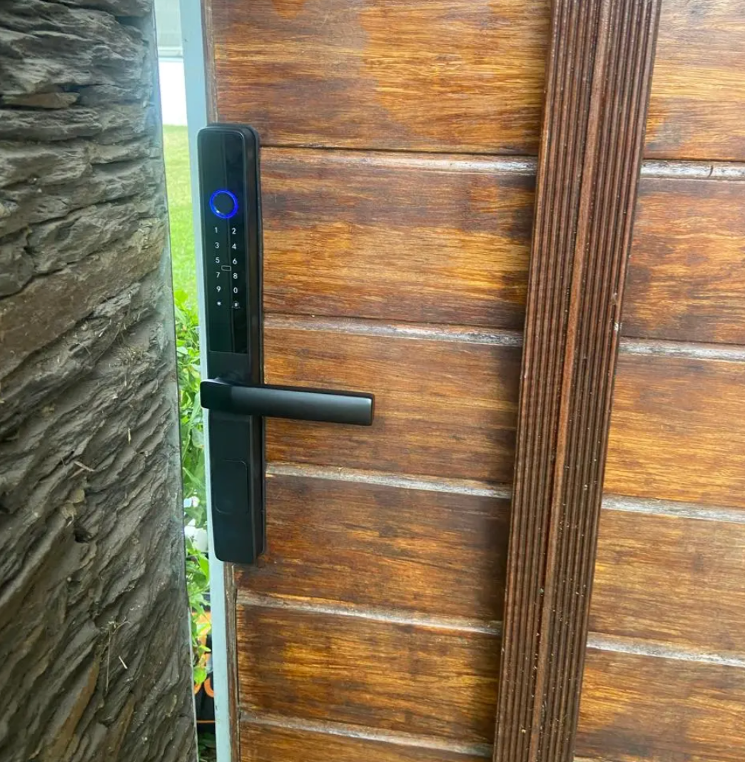 Black smart door lock fitted to a timber door beside stone cladding, seen from outside