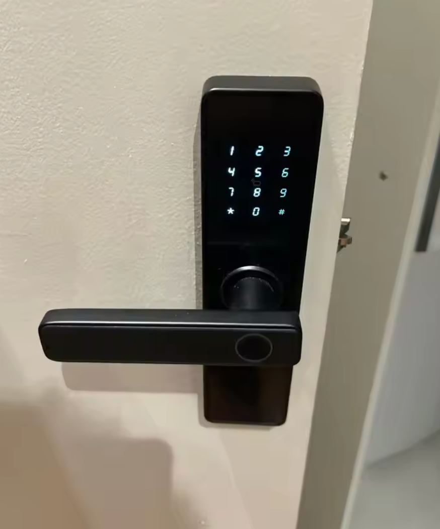 Black lever-handle smart door lock with the keypad lit, fitted to a white door